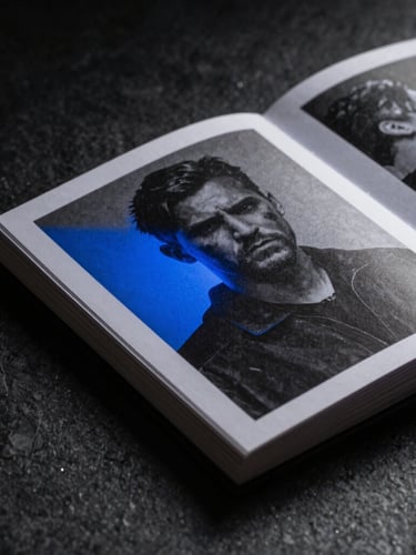 Extreme close-up macro detail of a high-concept physical campaign book on a dark stone table, dramatic low-key studio lighting with a sharp electric blue shadow casting across the textured paper.