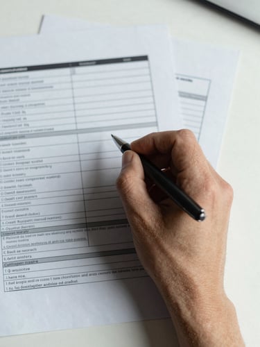 Extreme close-up overhead view of annotated credit analysis documents spread on a clean desk, a hand holding a pen mid-notation, north-facing daylight casting honest flat light across the papers, no faces visible