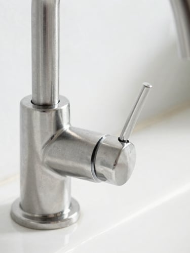 Detailed macro shot of a spotless stainless steel kitchen faucet, bright natural daylight reflecting off pristine metallic surfaces, sharp architectural focus