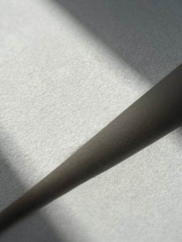 Close-up macro shot of structured heavy cotton paper with deep geometric shadows, cold natural light, minimalist and clean.