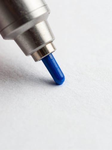 Extreme macro shot of a single laser-guided printing nozzle depositing vibrant blue ink onto textured white paper, high contrast studio lighting, 85mm lens