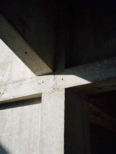 Macro detail of hand-carved wood joint meeting raw textured concrete, deep architectural shadows, strong directional sunlight, high-contrast chiaroscuro, 35mm film