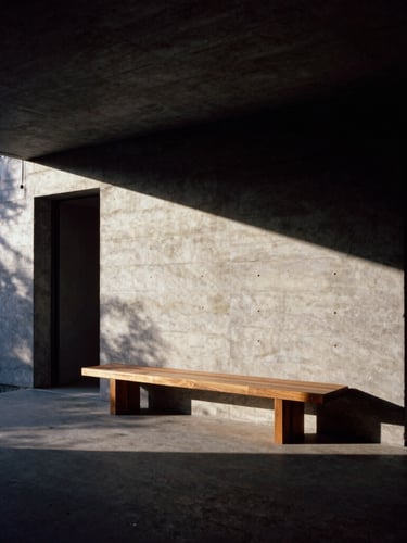 Dramatic wide-angle architectural shot of a raw concrete home at dusk, deep directional light casting long shadows across a bespoke walnut bench, 35mm film.