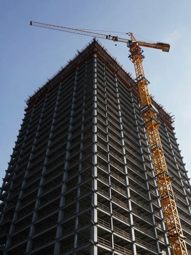 Low-angle heroic shot of a massive steel-framed high-rise construction site, crane silhouetted against high-contrast morning sky