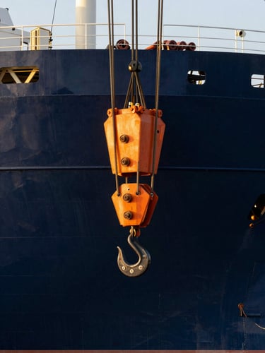 Close-up of industrial rigging on a heavy-lift vessel, massive steel cables and hooks securing cargo under crisp daylight, deep navy hull in background