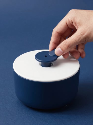 Close-up of a hand unboxing a clever minimalist kitchen gadget under bright studio lighting, clean navy blue background