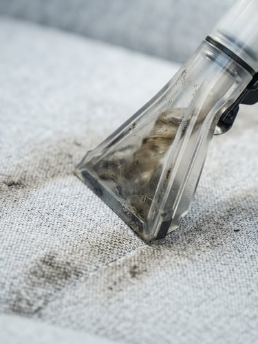 Macro shot of a high-tech extraction nozzle pulling deep-seated dirt from a light grey luxury fabric, bright daylight, clinical precision, 35mm