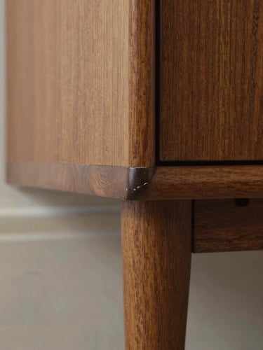 Macro detail shot of a subtle scuff on the wooden leg of a mid-century modern cabinet, soft studio lighting highlighting the texture of the wood grain and imperfection, neutral background, 50mm lens