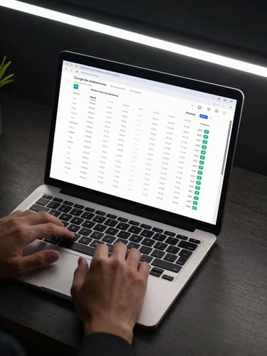 Wide shot of a dark office desk, laptop screen showing a Google Ads performance dashboard with ROAS columns and conversion data, hands resting on keyboard, cool LED overhead lighting, no faces visible, taken from slightly above