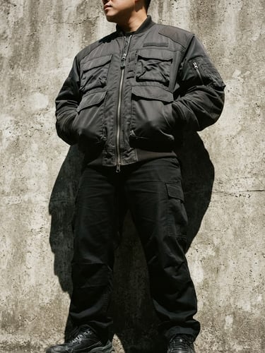 Low-angle heroic shot of a structured streetwear jacket against a textured concrete wall, sharp direct sunlight casting deep shadows, desaturated tones, 35mm lens.