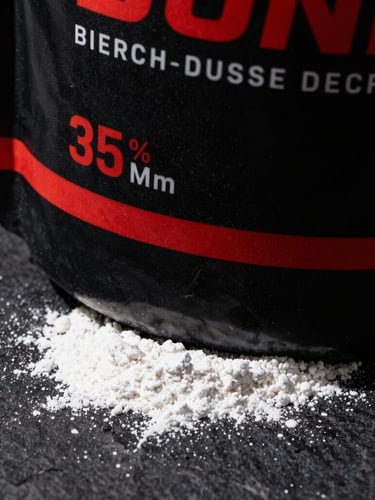 Tight close-up of premium black supplement packaging with sharp crimson accents, dramatic key lighting, raw white powder texture visible on a dark stone surface, 35mm lens