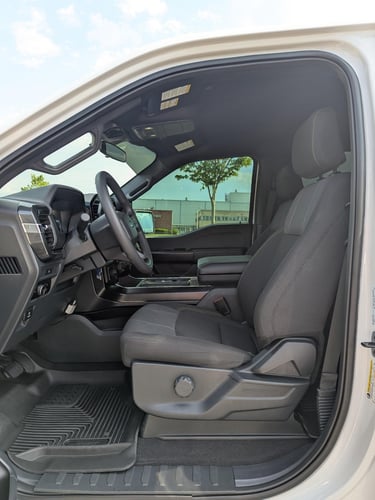 Interior view of a modern white Ford F-150 truck featuring black cloth seats and a leather steering wheel.