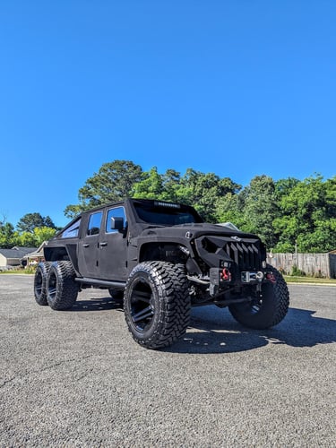 A matte black Apocalypse 6x6 truck with off-road tires parked on a sunny street.