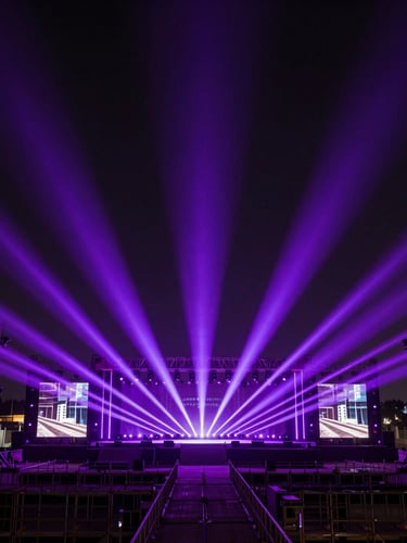 Extreme wide-angle shot of a massive corporate stage under construction, glowing with sharp purple laser beams and violet spotlights cutting through deep shadows, industrial metal scaffolding visible, cinematic composition.