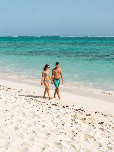 A wide-angle shot of a couple walking freely along a white-sand beach in Isla Mujeres, bright tropical sunlight, turquoise water in the background.