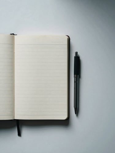 Overhead flat-lay of an organized desk: open planning notebook, ruled pages visible, a single pen resting beside it, cool north-facing daylight from the left, minimal negative space to the right, no hands, no faces