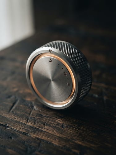 Macro close-up of a machined aluminum dial glowing softly on an oak desk under low-key side window light, shallow depth of field