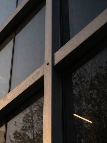 Extreme close-up of architectural steel and dark glass angles, dramatic low-key lighting with subtle golden reflections, clean minimalist composition.