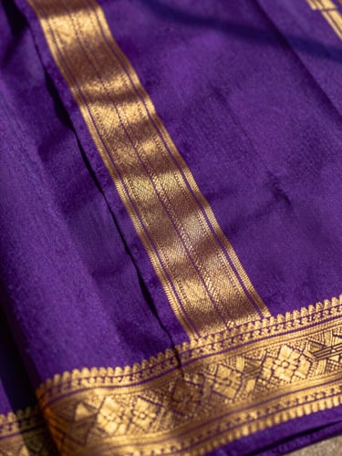 Macro close-up shot of raw silk saree texture, showing intricate golden zari border details, high-contrast natural sunlight, rich saturated jewel tones, 35mm.