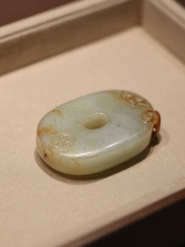 Macro close-up of ancient jade with soft side-light, showing rich patina, resting on a silk scholar's tray, warm scholarly setting, muted tones.