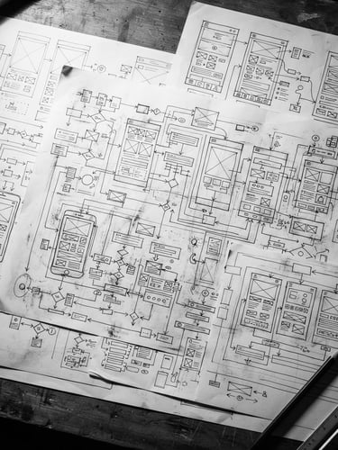 Stark monochrome overhead flat-lay of complex user flow schematics and wireframe blueprints on a drafting table, hard direct light, sharp shadows, macro lens, high contrast