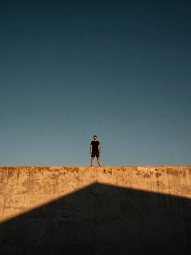 Wide environmental shot of a solitary figure standing at the edge of a massive concrete architectural ledge, open sky, dramatic shadows, athletic energy