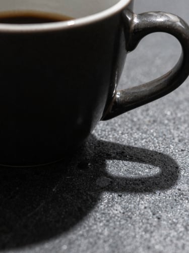 Macro close-up of a sleek dark ceramic espresso cup on an obsidian stone desk, dramatic side lighting, deep sharp shadows, premium minimalist aesthetic