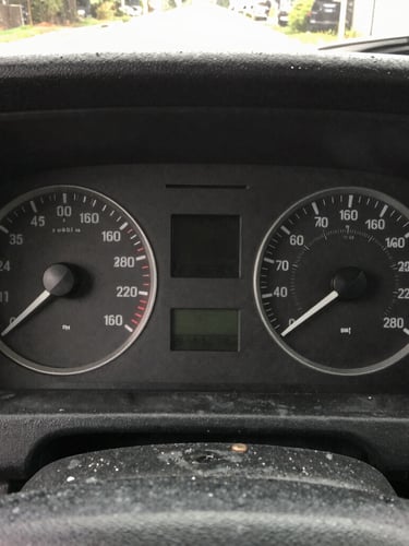 Close-up of a transit bus dashboard instrument cluster, sharp focus on dials and digital readout, early morning garage lighting, natural gritty colors