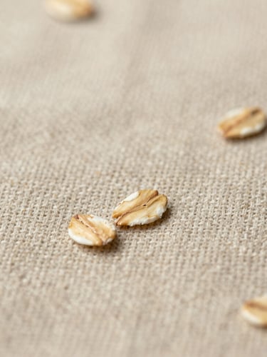 Extreme close-up of textured oatmeal linen weave, showing the beautiful imperfections of raw natural fibers in soft diffused light, warm editorial photography.