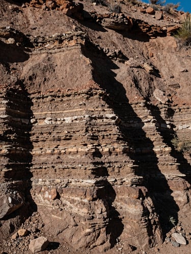 Close-up of raw desert soil and stone strata in Tucson, high-contrast side lighting revealing tectonic layers.