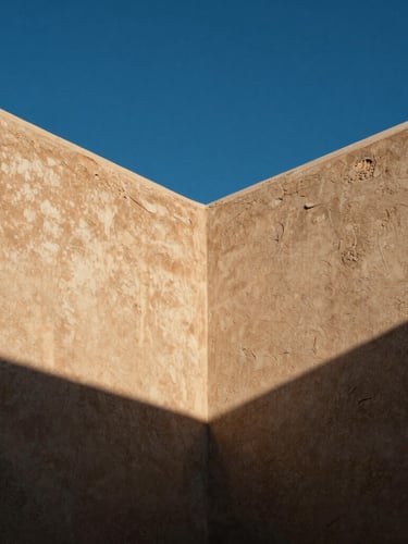 Low-angle shot of weathered stucco walls meeting a deep blue desert sky, sharp architectural shadows casting heavy lines, high-contrast midday sun.