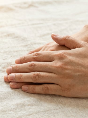 Close-up of two hands resting gently together on a soft linen tablecloth, warm diffused afternoon light, expressing care and quiet support, shallow depth of field.