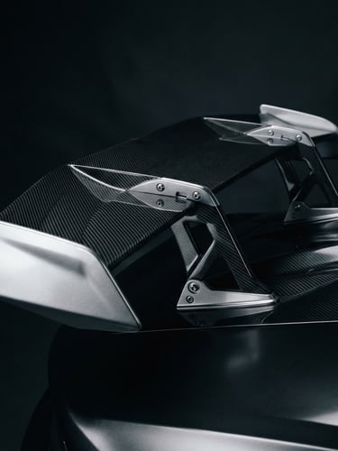 Low-key dramatic studio lighting on a sleek carbon-fiber supercar rear wing, sharp angles, metallic silver reflections, 35mm anamorphic