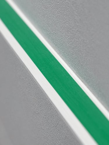 Macro close-up of a laser-straight green painter's tape line being peeled from a crisp slate grey wall, revealing a flawless stark white trim edge under bright daylight.