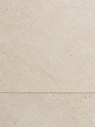 Close-up overhead shot of travertine tile surface, natural vein detail and pitting visible, raking side light revealing surface texture, grout line running along lower third, earthy cream and grey tones, no tools or hands