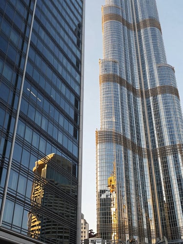 Low angle shot of modern architectural glass facades in Downtown Dubai, crisp daylight with gold highlights, deep navy reflections, sharp architectural focus, 35mm