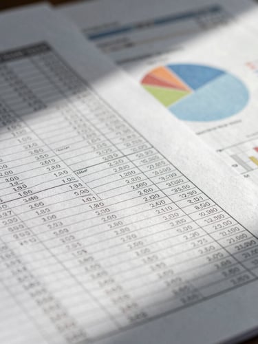 Tight macro detail of structured financial ledger sheets and analytical charts under cool overhead daylight, sharp focus, high contrast, showing no text details.