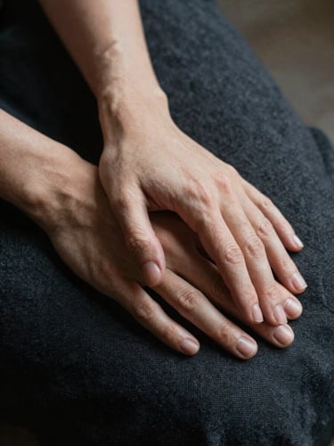 Close-up of hands resting calmly on a dark linen surface, soft natural side light, showcasing organic textures and a quiet moment of pause.
