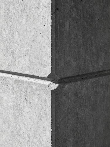 Macro shot of a concrete joint with hard directional lighting, sharp shadows, orthographic framing, high-contrast black-and-white.