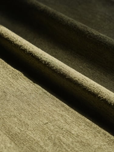 Close-up of structured olive-toned hemp fabric texture, sharp architectural folds, low-angle direct sunlight, dramatic shadows, 35mm film style.