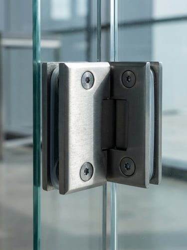 Macro close-up of a heavy-duty brushed stainless steel glass hinge mounted on a thick tempered glass panel, sharp architectural daylight, high-contrast shadows highlighting the metallic grain, 50mm lens.