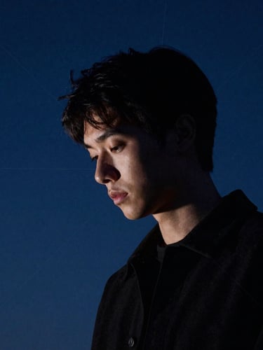 A thoughtful, introspective portrait of a person looking downward in deep contemplation, high-contrast chiaroscuro lighting, soft starlight from the side, deep slate blue background, fine-art photography
