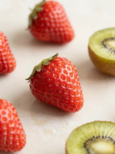 Macro shot of fresh whole strawberries and sliced kiwis on a warm cream marble surface, soft morning daylight, pastel tones, elegant composition