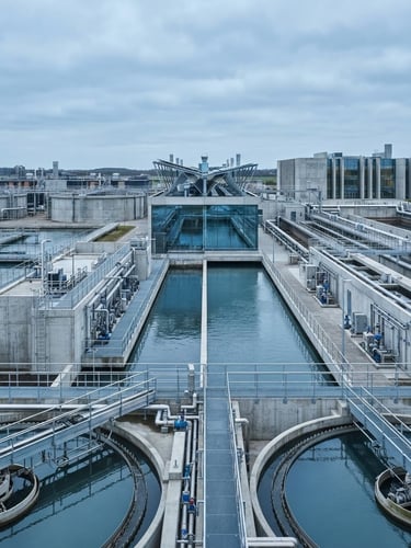 Wide-angle architectural photograph of a modern water treatment facility under overcast daylight, clean concrete structures, blue sky reflections, high technical detail.
