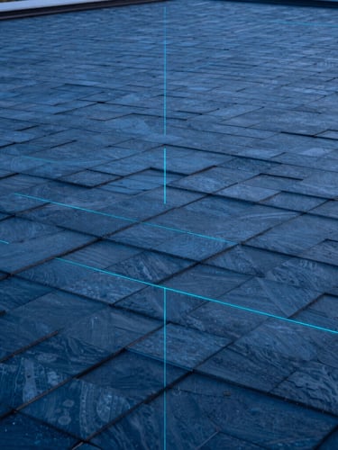 High-angle architectural blueprint-style rendering of a modern geometric roof with perfectly aligned slate-blue shingles, cool twilight lighting, sharp cyan grid lines.