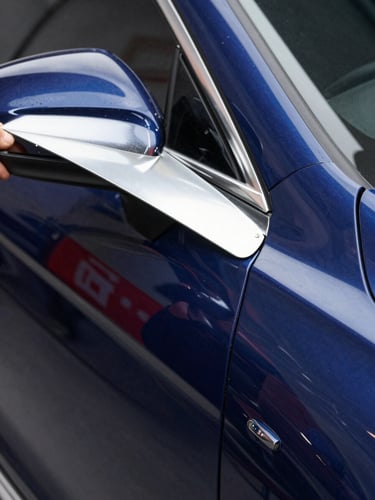 Close-up macro shot of a technician using specialized LED reflection boards on a clean navy blue car panel, sharp linear reflections showing perfect curves