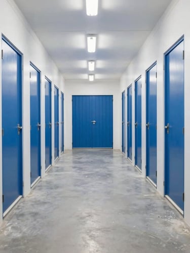 Straight-on symmetrical wide shot of a brightly lit, clean Dubai storage facility corridor with uniform blue doors and concrete floor.