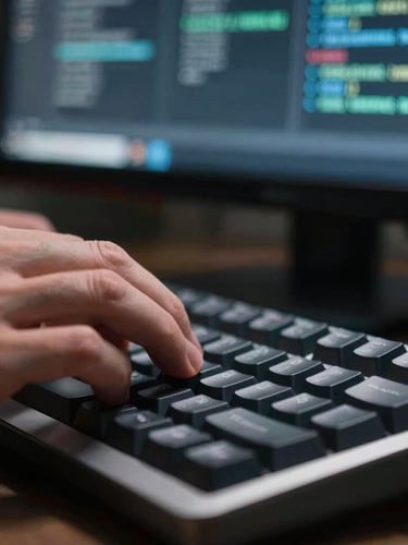 Macro shot of hands on a mechanical keyboard under sharp side-lighting, terminal code visible on a dark monitor in the background, 35mm lens.