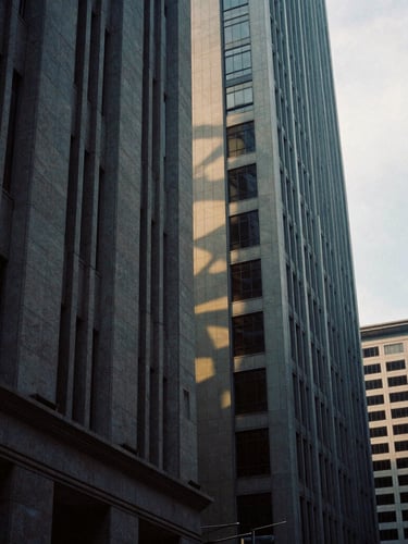 Abstract architectural details of Singapore's financial district, towering stone facades with deep dramatic shadows, soft overcast daylight, 35mm