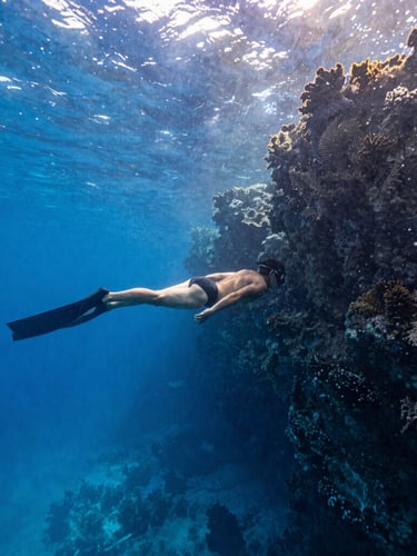 Wide-angle shot of a diver in perfect horizontal trim drifting along a deep blue vertical reef wall in Cozumel, sunbeams piercing the crystal clear water